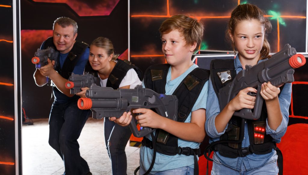 Smiling kids and parents with laser guns and playing together laser tag game indoors.