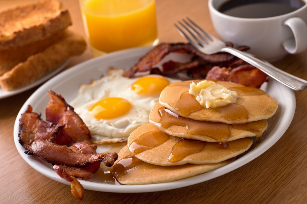 A delicous home style breakfast with crispy bacon, eggs, pancakes, toast, coffee, and orange juice.